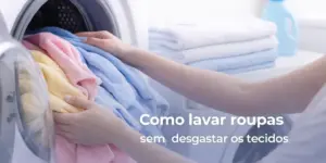 Pessoa coloca toalhas coloridas na máquina de lavar roupa com detergente ao fundo